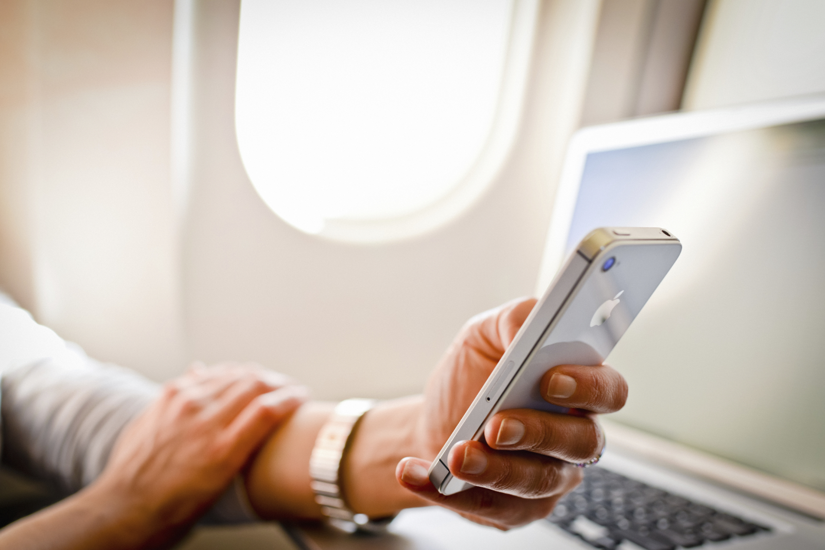 Woman using iPhone 4s and laptop in airplane during flight